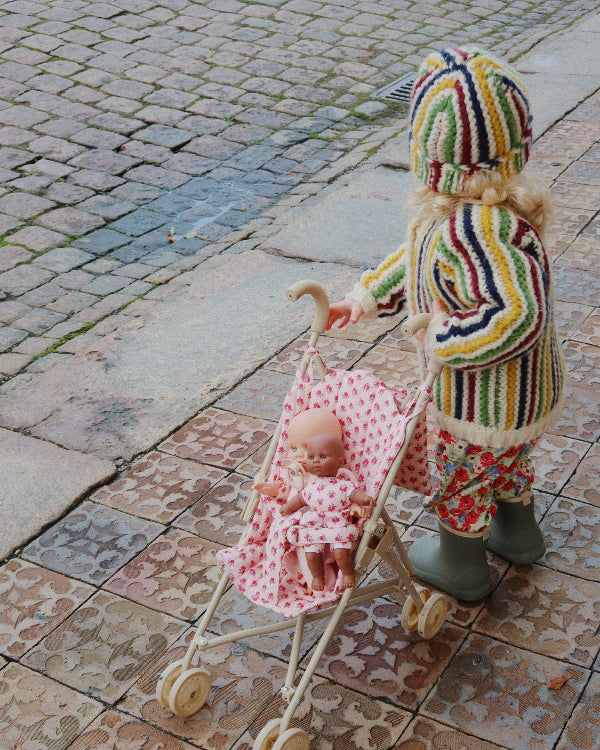 Child in colorful outfit pushing a baby in a stroller on a cobblestone street
