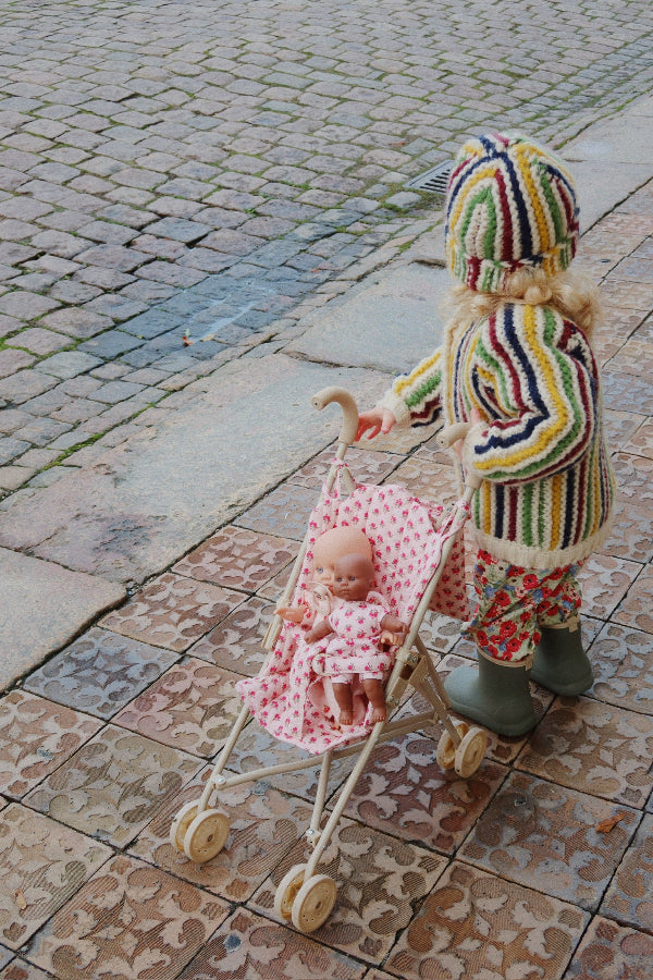 Child in colorful outfit pushing a baby in a stroller on a cobblestone street