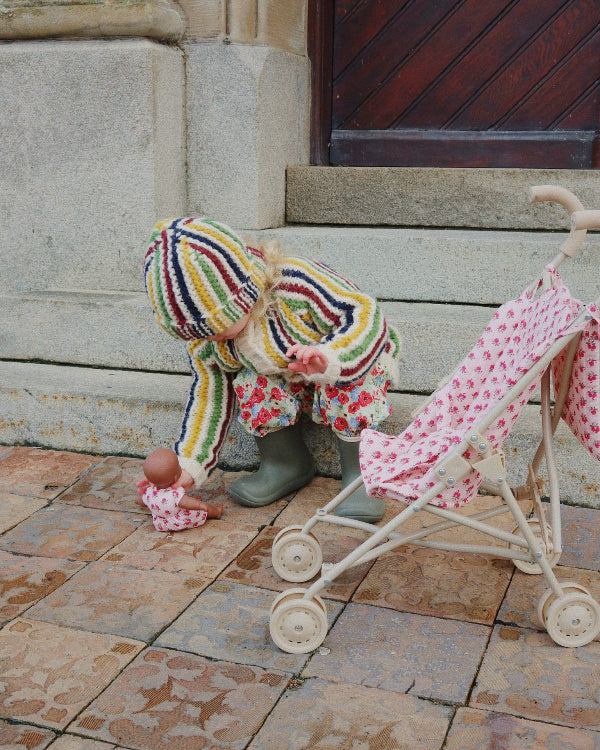 Child in colorful outfit playing with a baby doll and pink stroller on stone pavement.