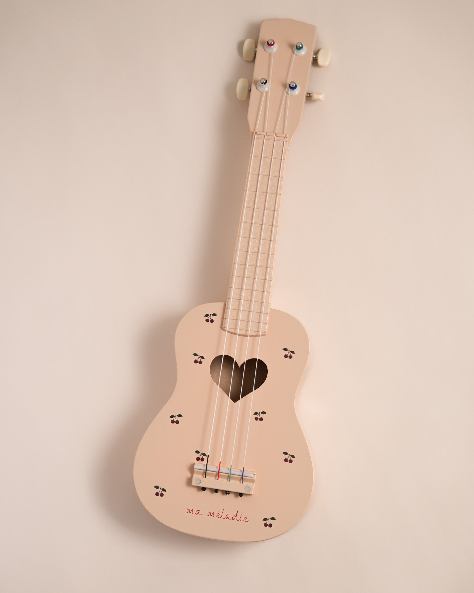 Cherry print wooden ukulele with heart sound hole and 4 nylon strings on neutral background