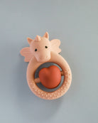 A silicone teether designed as a unicorn with a rose sand color heart-shaped element in the center, presented against a blue background.
