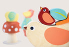 Colorful wooden toys including a bird, mushroom, and leaf on a light background