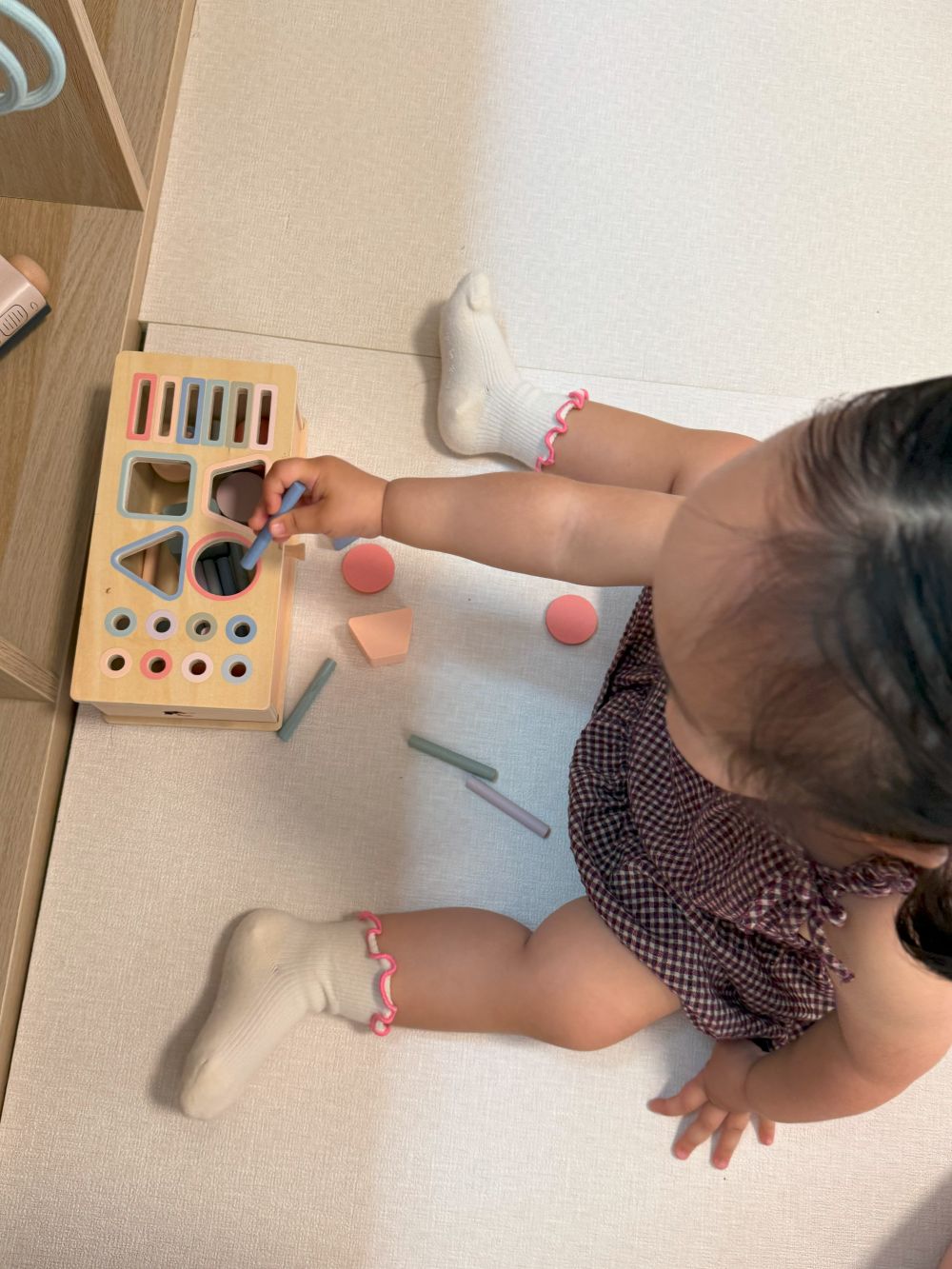 Child playing with a shape sorting toy on a light-colored floor.