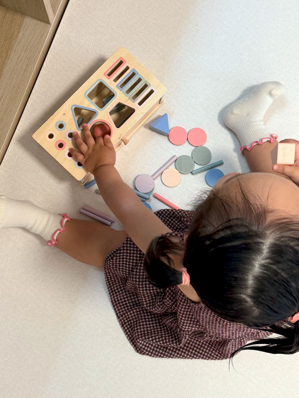 Child playing with a shape sorting toy on a light-colored floor.