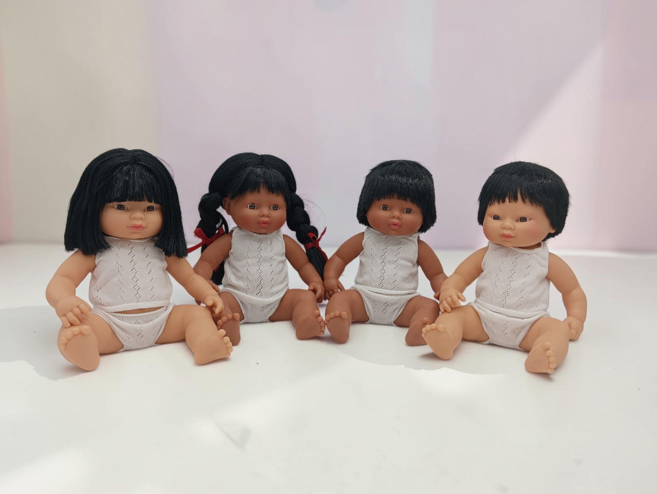 Four dolls with black hair and white outfits sitting on a light surface.