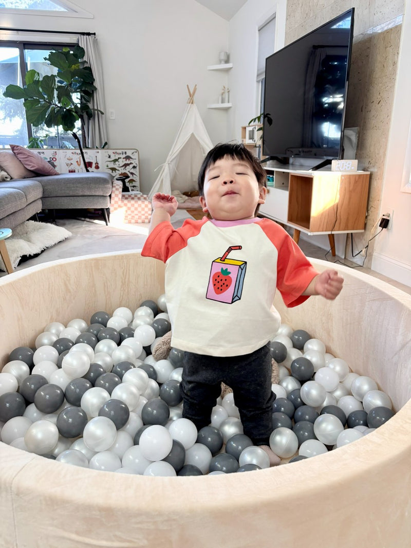 Child playing in a ball pit with a colorful bib in a living room.