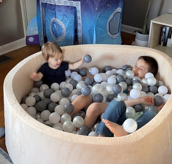 Two children playing in a ball pit with colorful balls inside a room.