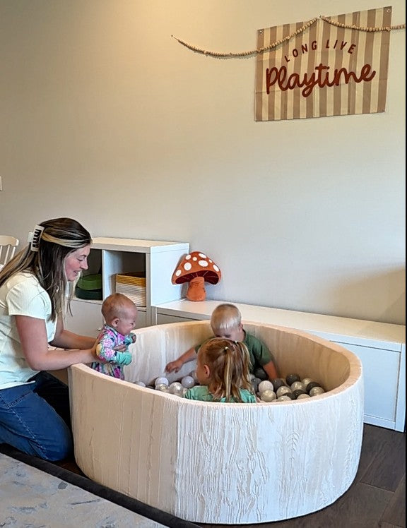 Children playing in a modern play area with a woman supervising, featuring a mushroom decoration on the wall.
