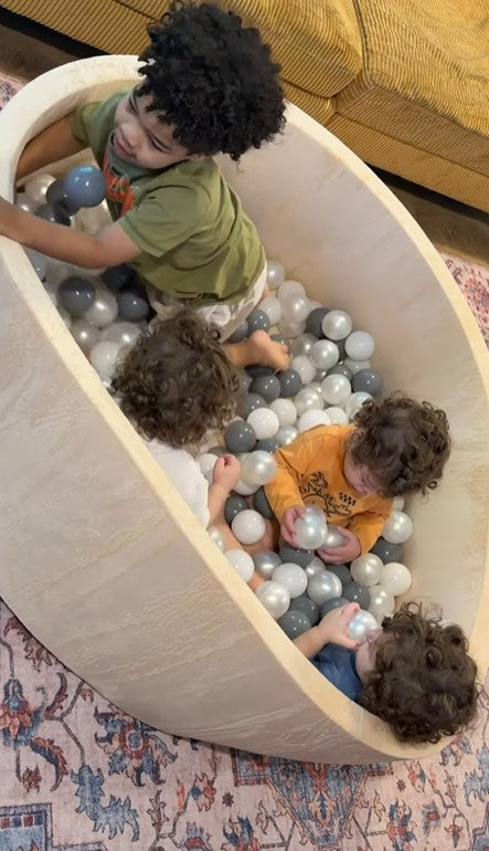 Children playing in a ball pit with colorful balls inside a wooden structure.