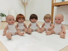 Five baby dolls with different hair colors sitting on a white mat.