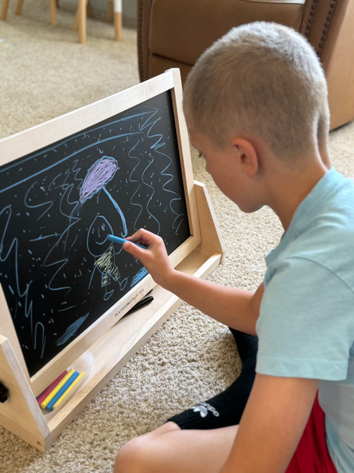 Child drawing on a blackboard with a blue marker indoors.