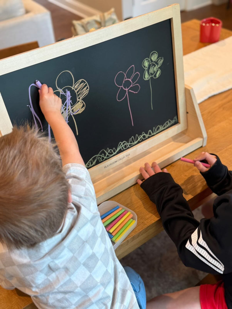 Two children drawing on a small chalkboard with colorful chalks.
