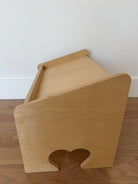 Wooden pet bed with a heart-shaped opening on a wooden floor.