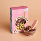 Tiny Harlow cereal box with a bowl of cereal and spoon on a beige background