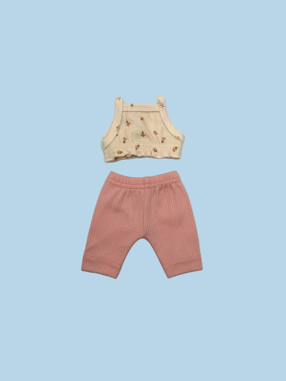 A two-piece baby outfit set laid flat on a light gray background, featuring a cream-colored sleeveless top with a small brown floral pattern and matching pink ribbed shorts.