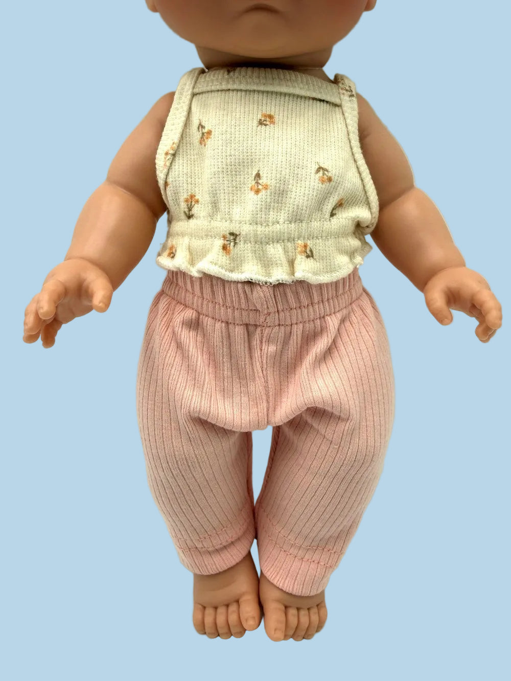 A doll or toy figure wearing a sleeveless cream top with small tan floral motifs and pink ribbed pants, photographed against a plain light background.