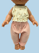 A doll or toy figure wearing a sleeveless cream top with small tan floral motifs and pink ribbed pants, photographed against a plain light background.