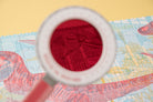 Red textured object under a magnifying glass on a colorful map background
