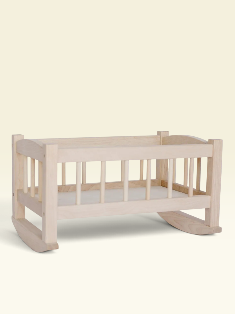 A light natural wood baby rocking cradle with vertical slats and a white mattress, shown against a solid pale cream background.