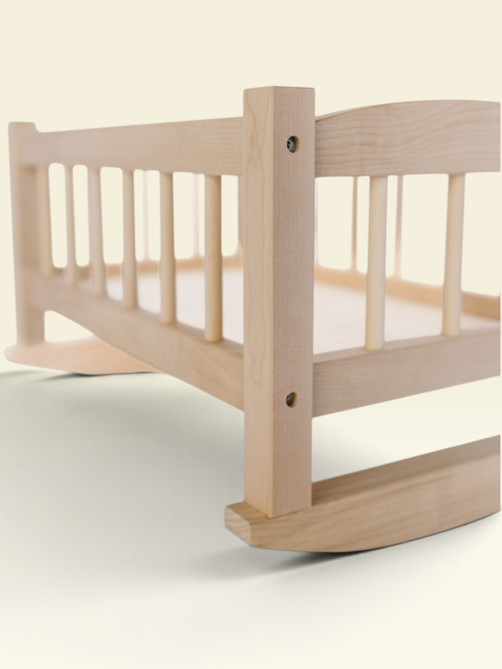 A close-up of a light natural wood rocking bed frame, showing the slatted side rail, corner post, and curved rocker base against a soft cream background.