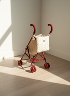 Red toy stroller with a white basket on a wooden floor.