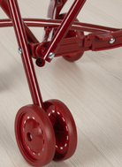 Close-up of a red metal stand with wheels on a light wooden floor.