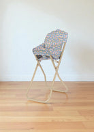 Side view of Fleur Rosier high chair showing foldable champagne metal frame in collapsed position for storage
