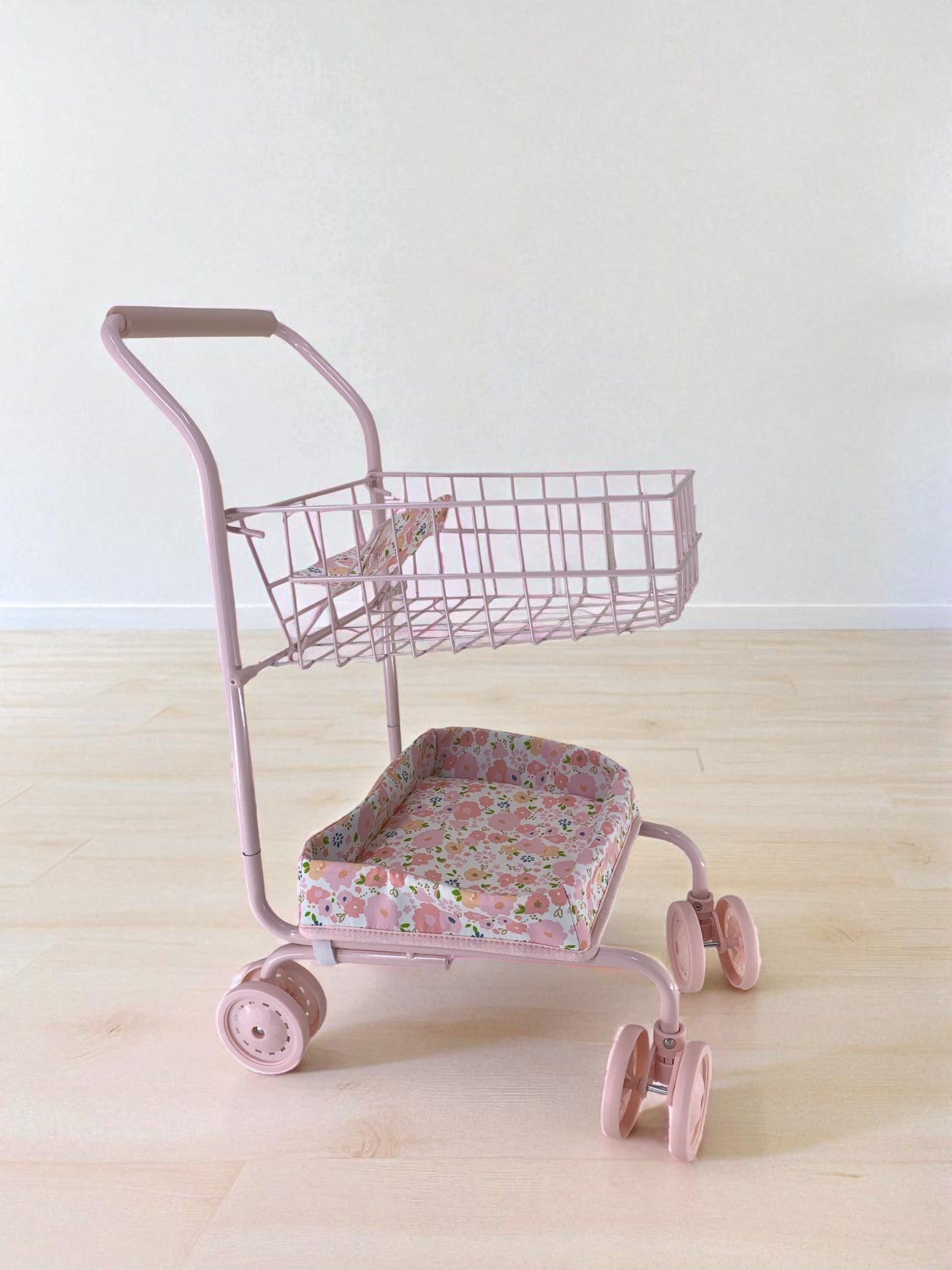 Side view of pink floral doll cart showing two-tier design with upper basket and padded lower seat platform