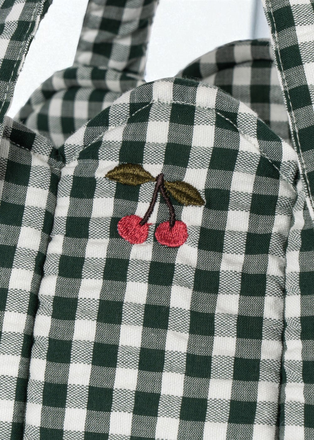 Close-up of embroidered cherry accent on green and white checkered bassinet showing charming decorative detail