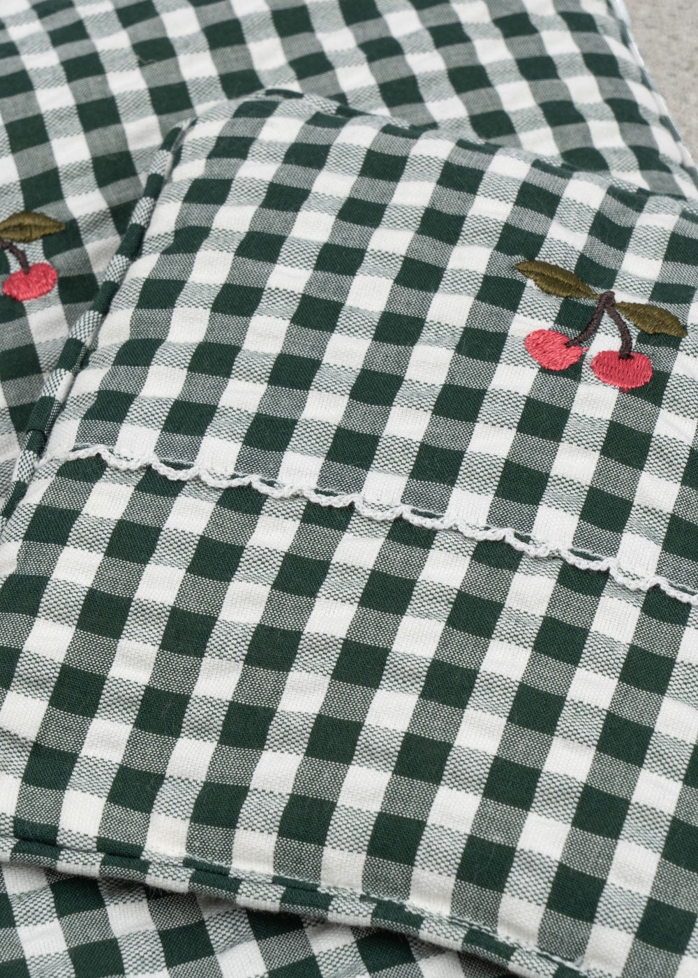 Close-up of embroidered cherry accent on green check bedding showing charming farmhouse decorative detail