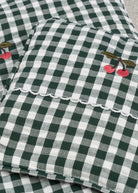 Close-up of embroidered cherry accent on green check bedding showing charming farmhouse decorative detail