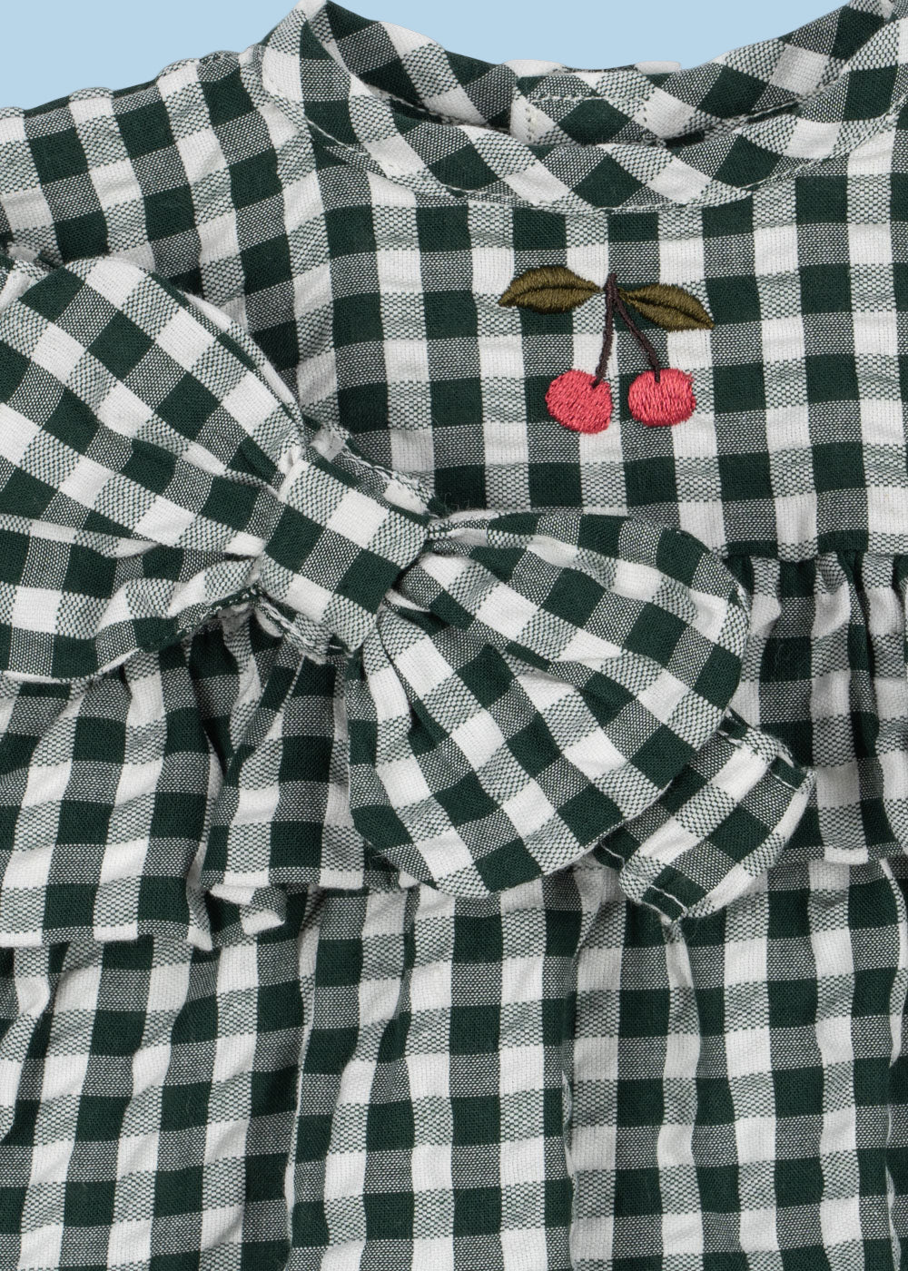 Close-up of embroidered cherry detail on green and white checkered doll dress bodice