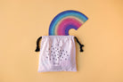Colorful rainbow-shaped object on a white drawstring bag with text against a beige background