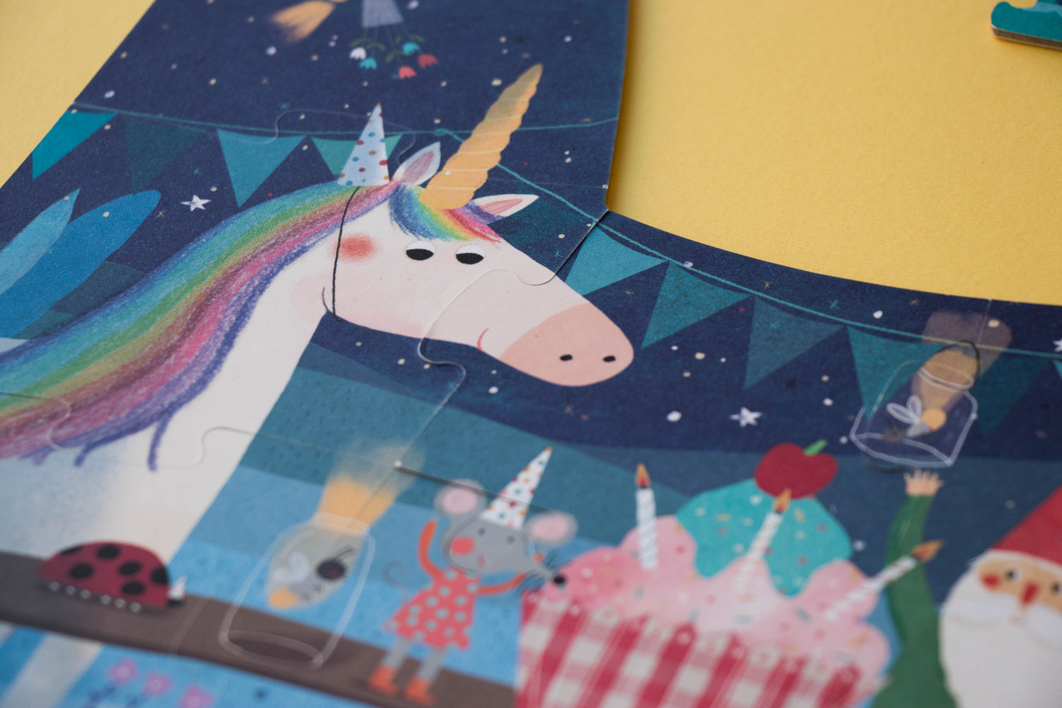 Children's puzzle with a unicorn, cake, and birthday-themed pieces on a blue and yellow background.