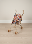 Small baby doll stroller with a colorful patterned cover on a wooden floor.
