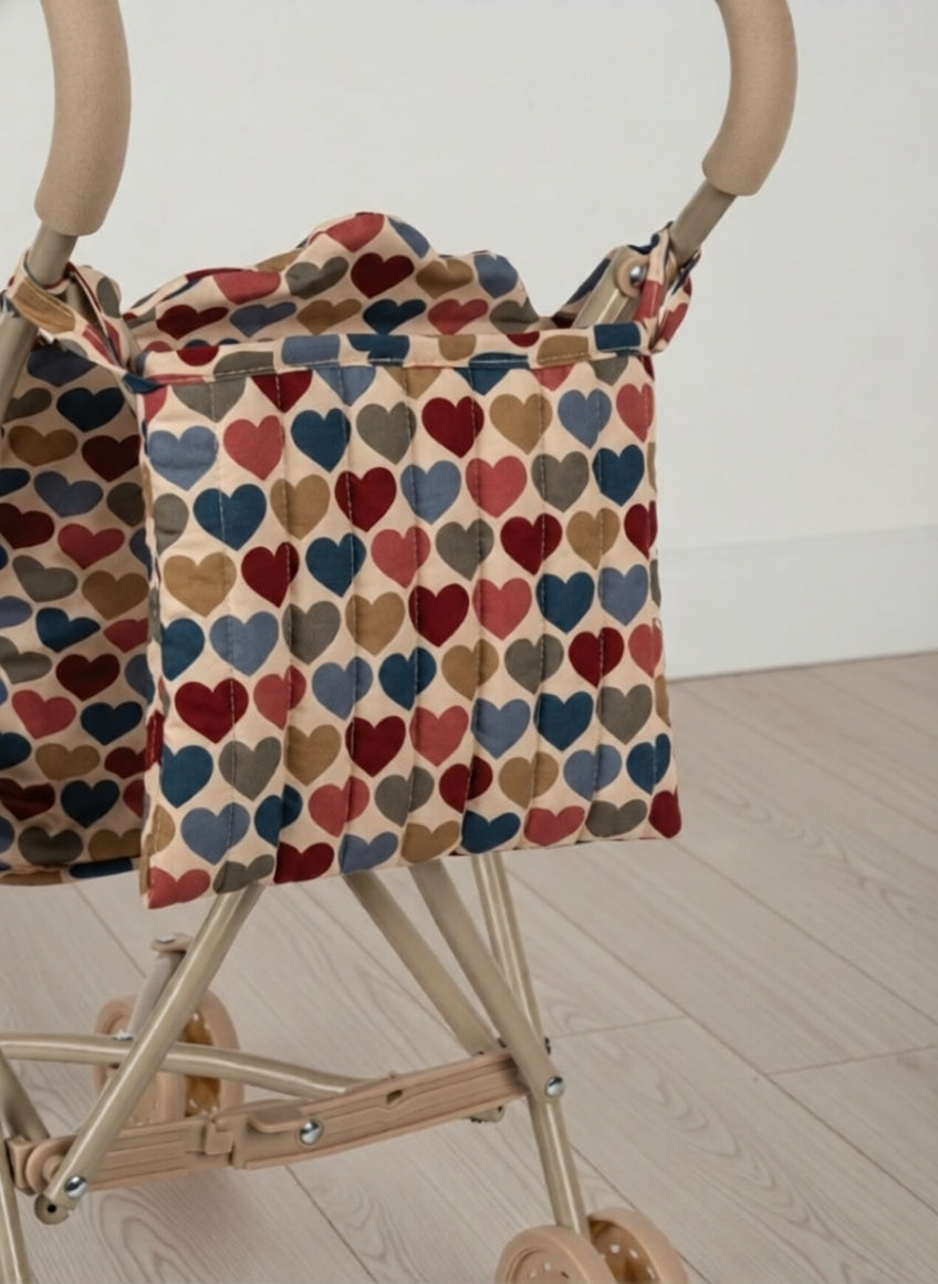 Stroller with a colorful heart-patterned cover on a wooden floor.