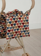 Stroller with a colorful heart-patterned cover on a wooden floor.