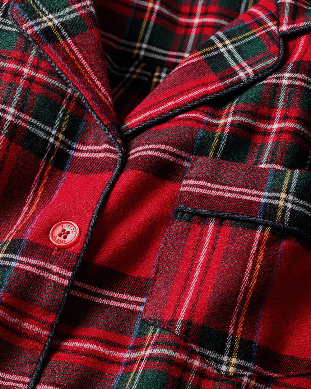 Close-up of red Imperial Tartan plaid flannel with navy piping and pearl button detail on children's pajamas