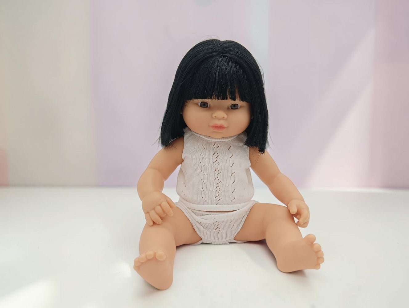 Doll with black hair wearing a white outfit on a light background
