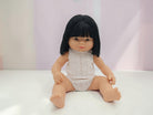 Doll with black hair wearing a white outfit on a light background