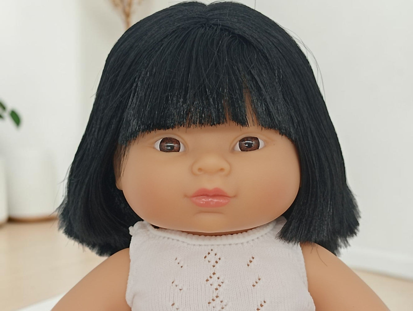 Doll with black hair and a white outfit against a neutral background