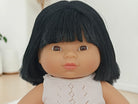 Doll with black hair and a white outfit against a neutral background