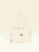 A cream-colored quilted bag with black polka dots and a small embroidered cherry motif on the front, featuring a matching shoulder strap and top handles, set against a solid cream background.