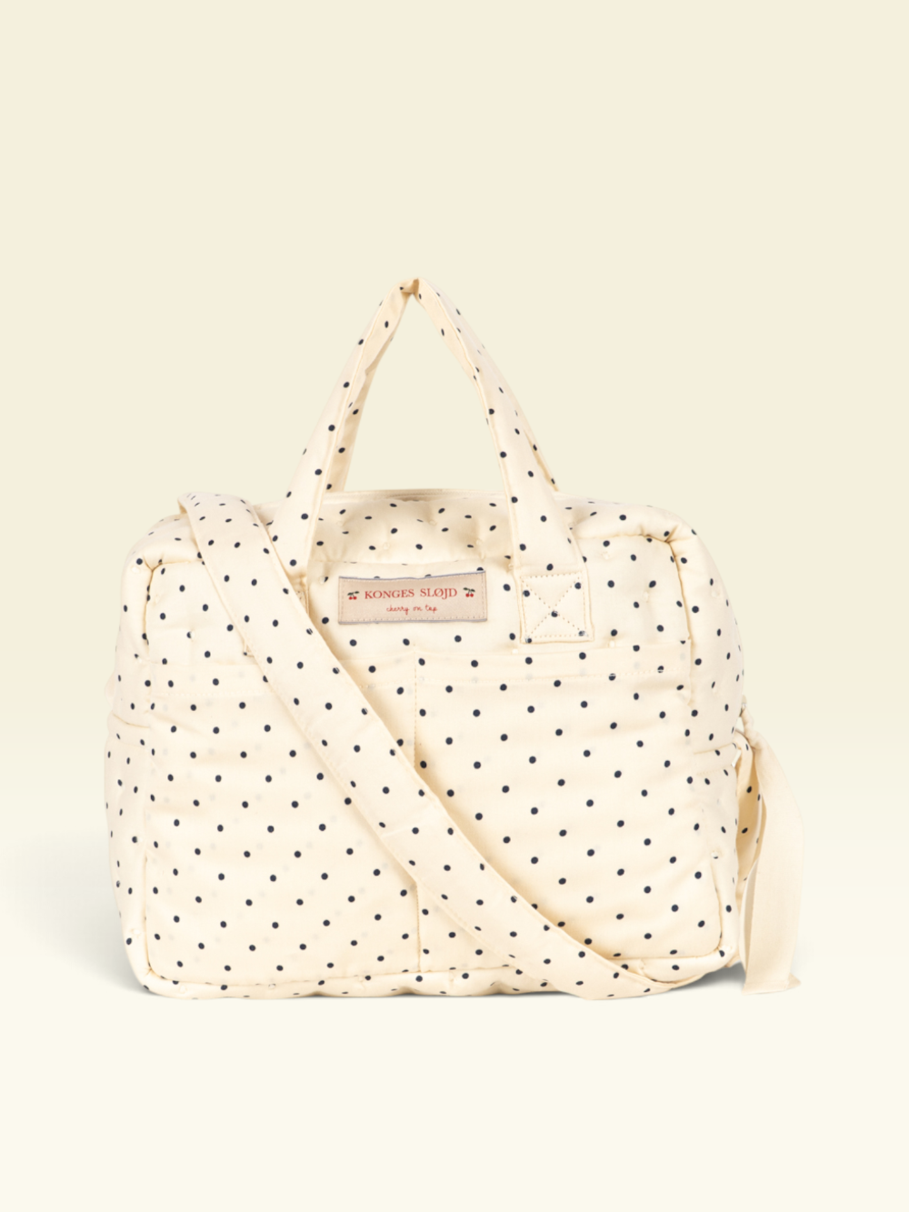 An off-white quilted duffel bag with black polka dots, featuring dual top handles, a detachable shoulder strap.