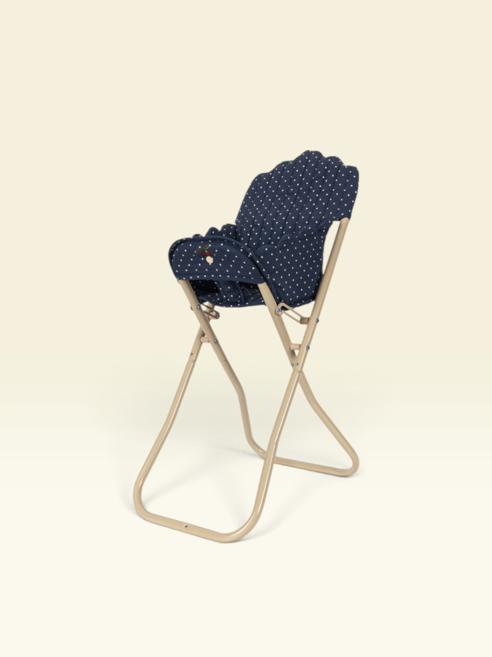 A folding chair with a beige metal frame and a navy blue fabric seat cushion featuring a small white polka dot pattern, shown against a solid cream background.