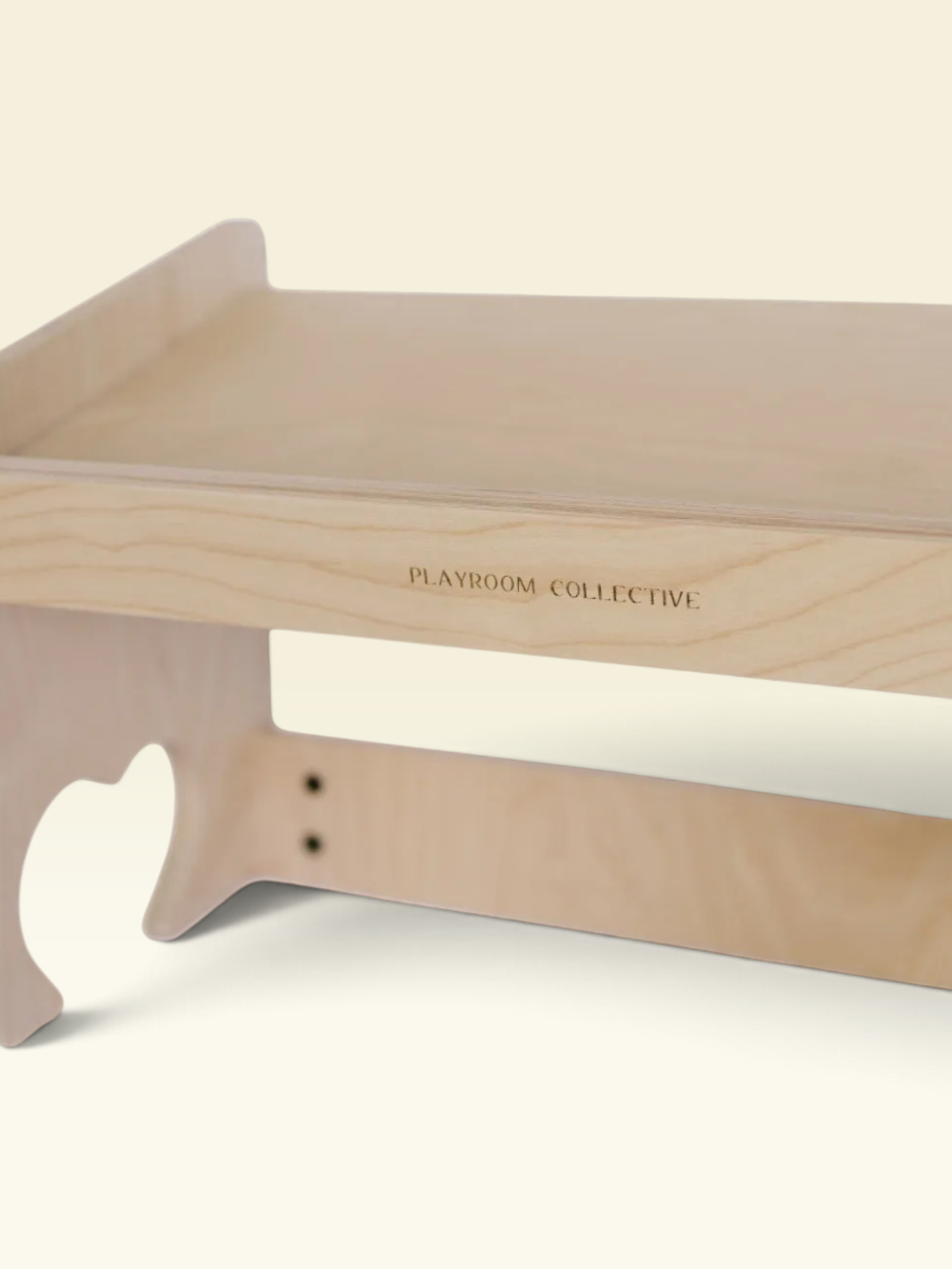 Close-up of a light natural wood playroom organizer or desk shelf with the brand name 'PLAYROOM COLLECTIVE' printed on the side, set against a solid cream background.