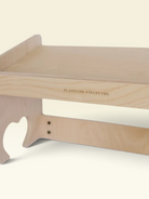Close-up of a light natural wood playroom organizer or desk shelf with the brand name 'PLAYROOM COLLECTIVE' printed on the side, set against a solid cream background.