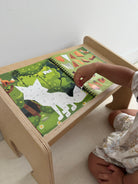 A child's hand placing a white animal silhouette piece onto a colorful wooden activity table with a green forest pattern