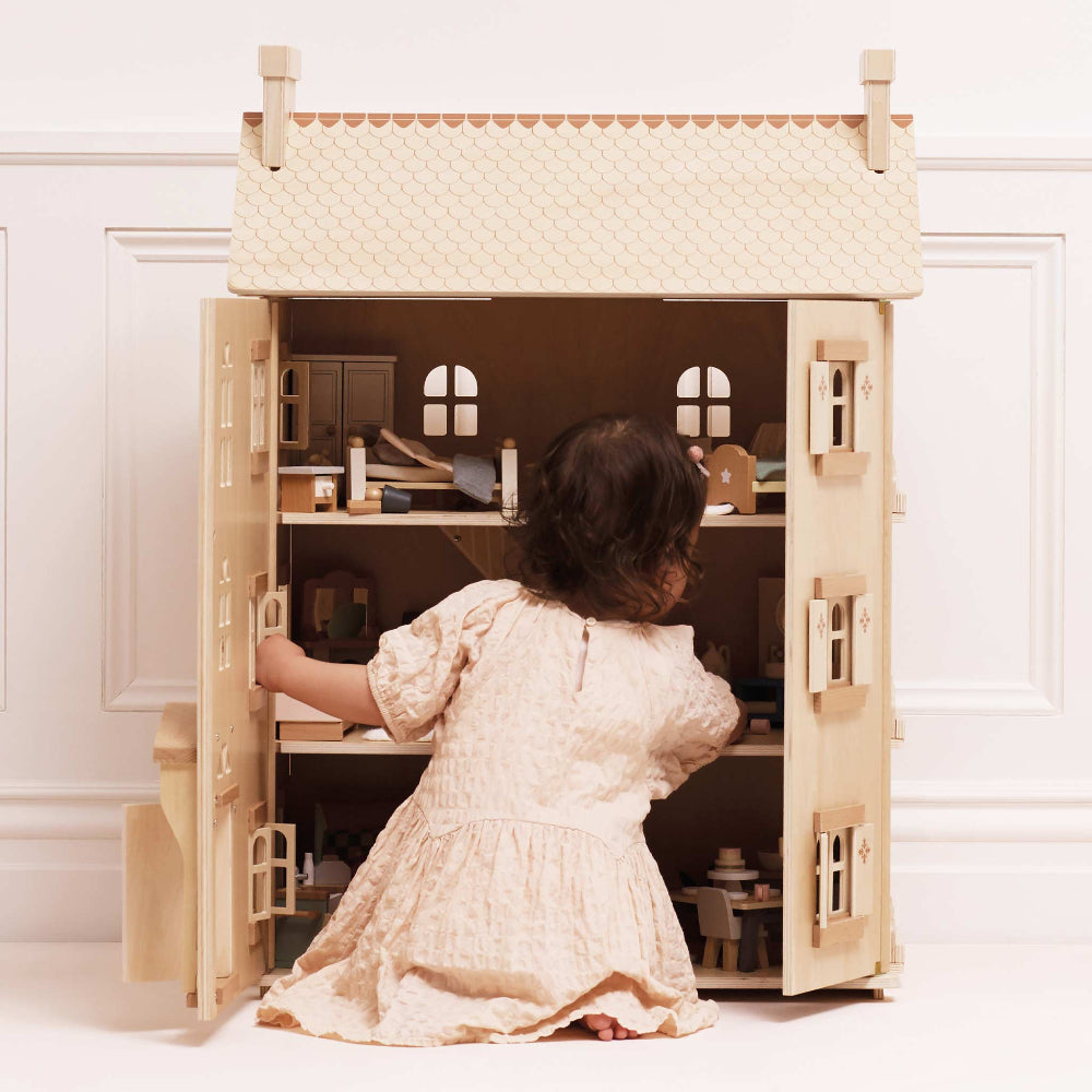 Child playing with a wooden dollhouse on a white floor.