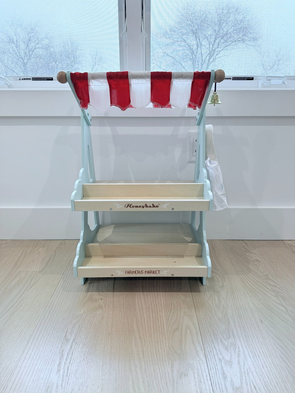 Wooden toy kitchen with red and white striped canopy on a light wooden floor.
